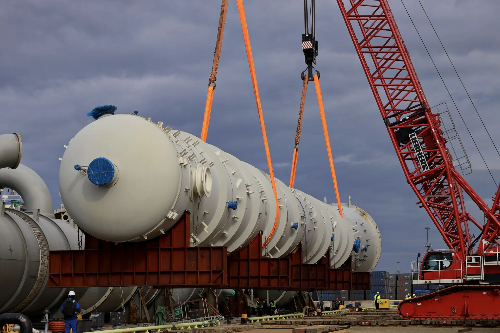 Close-up of oversized cylindrical equipment suspended from crane slings